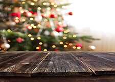 Decorated Christmas tree behind a rustic brown wood table.