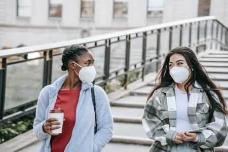 Two women wearing face masks walking outside.