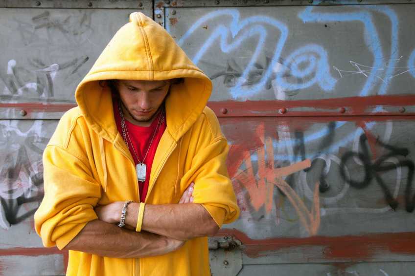 Young person in a yellow hoodie standing with his head down.