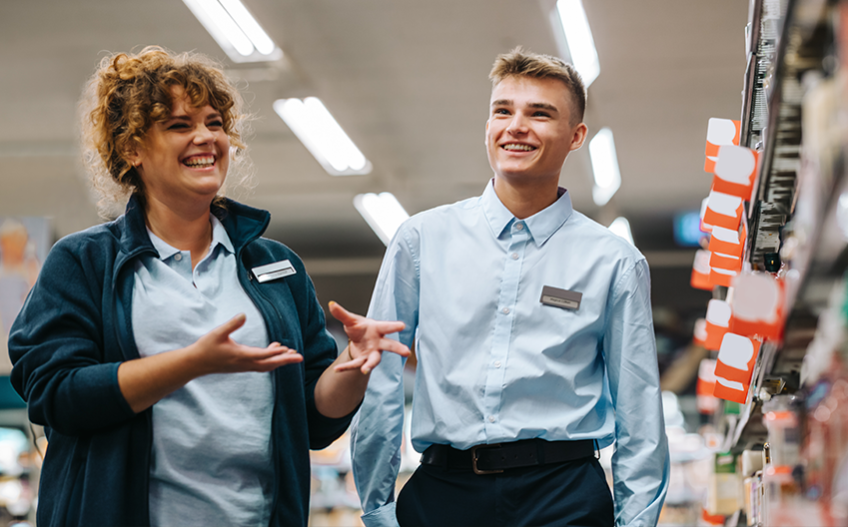 two retail workers, one women, one young man, smiling 