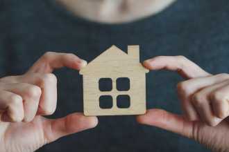 hands holding a piece of cardboard cut to be shaped like a house 